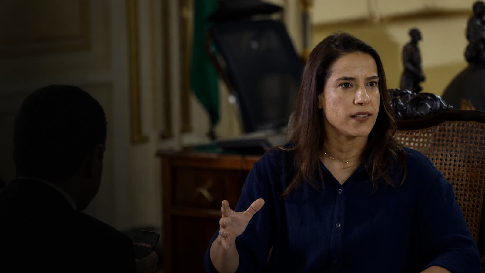 Montagem editorial mostra Raquel Lyra no Palácio do Campo das Princesas diante de um homem mantido sob sombra para representar um deputado não identificado